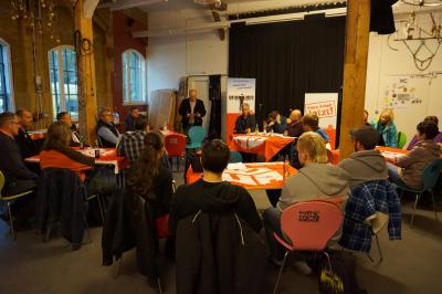 Das Centro Sociale mit Referenten und Publikum, im Hintergrund Banner der IG BAU.