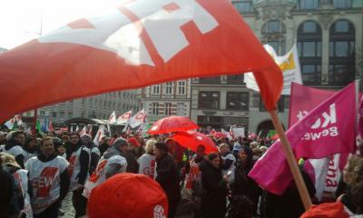 Demonstranten mit ver.di-Fahnen, im Vordergrund eine IG BAU-Flagge