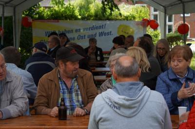 Rund 30 Menschen an Biertischen, im Hintergrund ein Transparent mit der Aufschrift: &quot;Wir haben es verdient - gleiche Löhne Ost und West!&quot;