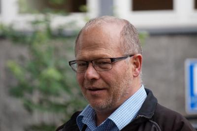 Nahaufnahme von Matthias Maurer, mit Brille und Kragen eines blau-weiß karierten Hemdes ... im Hintergrund ein Baum und ein Gebäude.