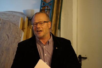 Ein 40 bis 50 Jahre alter Mann mit Brille, kariertem Hemd und Jackett bei einer Rede.