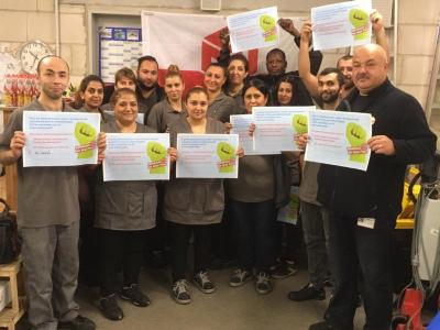 16 Menschen, Männer und Frauen, in grauer Arbeitskleidung stehen im Halbkreis vor einer Fahne der IG BAU und halten Plakate mit Tarifforderungen in die Kamera. 16 Menschen, Männer und Frauen, in grauer Arbeitskleidung stehen im Halbkreis vor einer Fahne der IG BAU und halten Plakate mit Tarifforderungen in die Kamera.