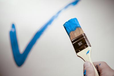 Pinsel mit blauer Farbe, blauer Haken auf weißer Wand Pinsel mit blauer Farbe, blauer Haken auf weißer Wand