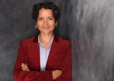 Tanja Chawla in rotem Oberteil vor einer grauen Wand. Tanja Chawla in rotem Oberteil vor einer grauen Wand.