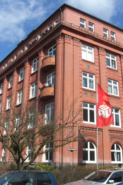 Das Bundeshaus der IG BAU in Hamburg - fünf Stockwerke, roter Backstein, davor rote Fahnen der IG BAU.
