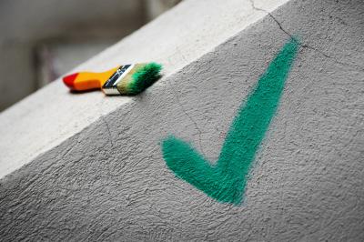 Mann im dunkelrotem Pulli, mit Mundschutz, Augen- und Gehörschutz, der mit Hammer und Meißel einen Stein bearbeitet.