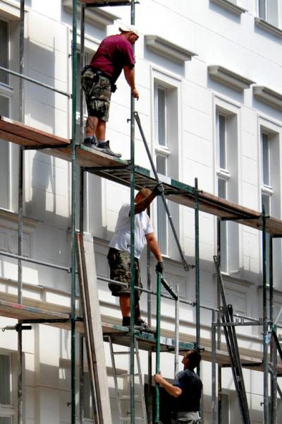 Gerüstbauer in Aktion, die sich Gerüstteile über drei Etagen zustecken.