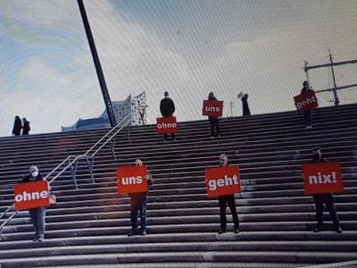 Ein halbes Dutzend Reinigungskräfte mit roten Schildern auf einer großen Treppe, im Hintergrund die Elbphilharmonie. Ein halbes Dutzend Reinigungskräfte mit roten Schildern auf einer großen Treppe, im Hintergrund die Elbphilharmonie.