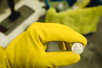 Euromünze in der Hand einer Reinigungskraft mit gelbem Gummihandschuh Euromünze in der Hand einer Reinigungskraft mit gelbem Gummihandschuh