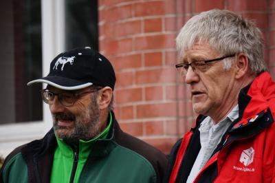 Zwei Männer, die in dieselbe Richtung blicken. Einer der Männer trägt eine schwarze Kappe und ein gründes Oberteil, der andere haut graue Haare und trägt eine rote IG BAU-Jacke. Zwei Männer, die in dieselbe Richtung blicken. Einer der Männer trägt eine schwarze Kappe und ein gründes Oberteil, der andere haut graue Haare und trägt eine rote IG BAU-Jacke.